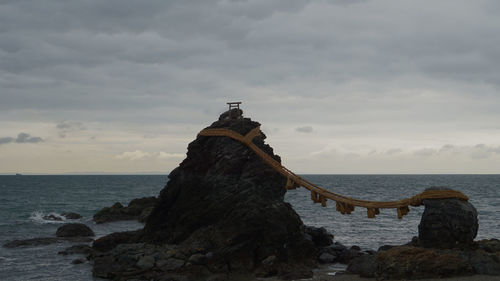 Cross on rock by sea against sky