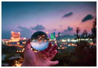 Close-up of hand holding crystal ball against sky