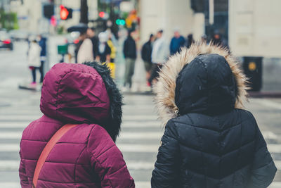 Two women wearing thick rainy day jackets with fur and people in the city