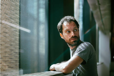 Mid adult man looking away while standing by apartment window