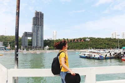 Woman standing by river in city against sky