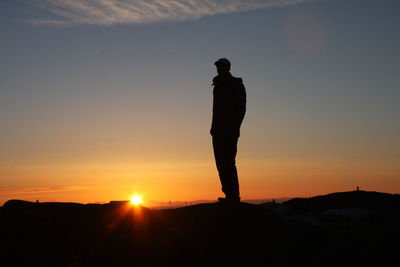 Silhouette man standing on landscape against sky during sunset