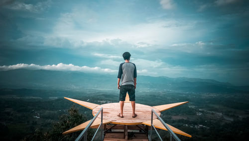 Rear view of man standing on mountain against sky