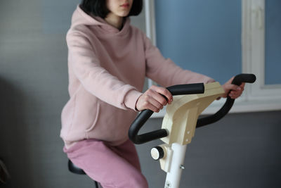 Midsection of woman holding bicycle standing against wall