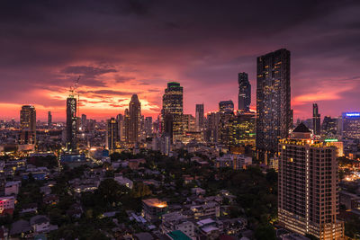 Illuminated buildings in city against cloudy orange sky at dusk