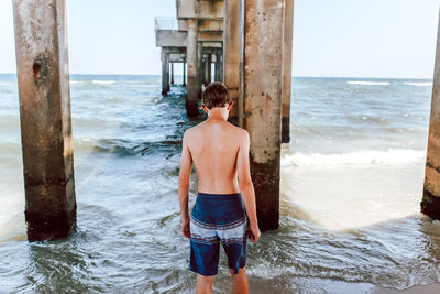 Man standing on wooden post at beach against sky