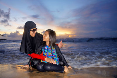 Women on beach against sky during sunset