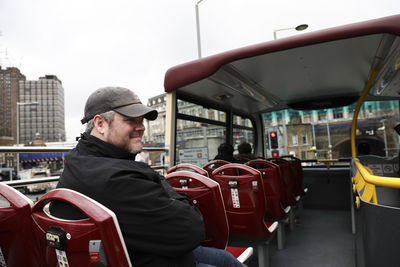 Happy man wearing jacket sits on top of double decker bus in london