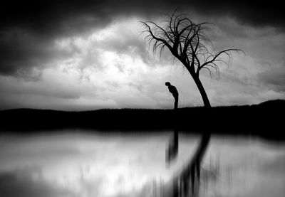 Bare trees on landscape against cloudy sky
