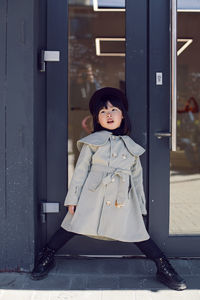 Korean girl in a gray coat and cap and round glasses stands the street in spring at the glass door