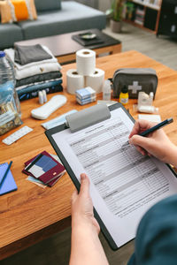 Unrecognizable woman doing checklist of emergency backpack in the living room