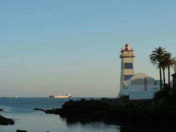 Lighthouse on calm sea against clear sky
