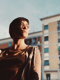 Low angle view of thoughtful young woman against buildings