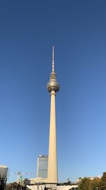 Low angle view of communications tower in city against clear blue sky