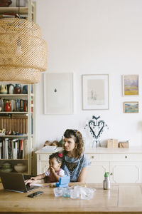 Woman using laptop while sitting with daughter at table in house