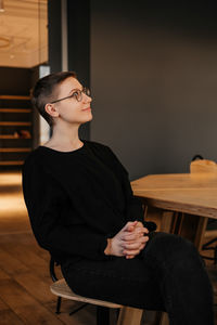 Young woman with short hair in eyeglasses and black sweater sitting at the table in office