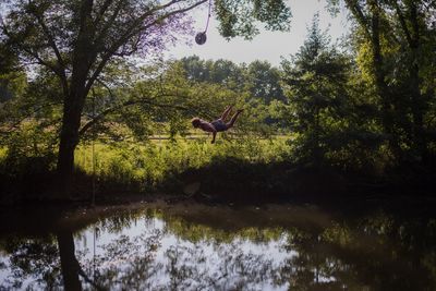 Man jumping over pond against trees