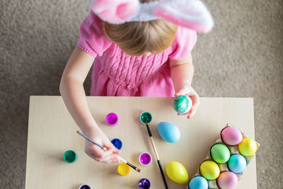 Little girl in easter bunny ears painting colored eggs. easter family holiday celebration at home.