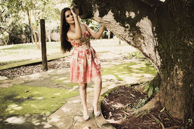 Portrait of beautiful woman standing by tree trunk