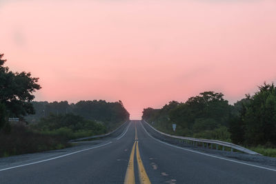 Road amidst trees against sky during sunset