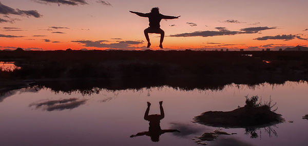 Silhouette man standing by lake against sky during sunset