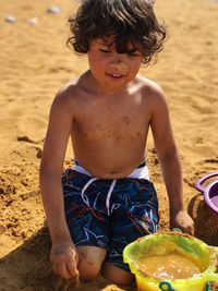 Playful shirtless boy with toys at sandy beach on sunny day