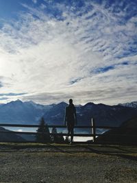 Rear view of man standing on snowcapped mountain against sky