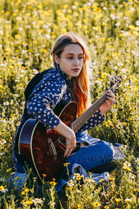 Young woman holding guitar on field
