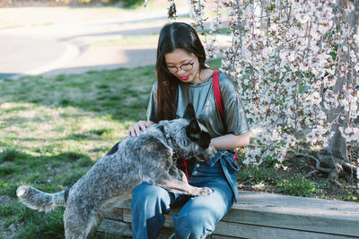 Young woman with dog sitting against tree trunk