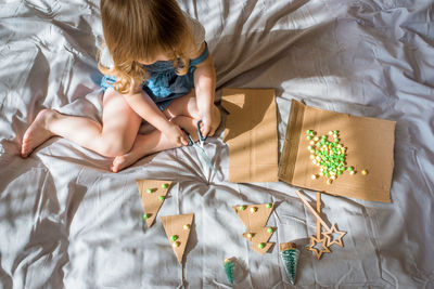 High angle view of girl playing with decoration while sitting on bed