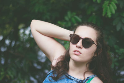 Portrait of young woman in sunglasses against tree