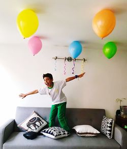 Full length of man holding balloons against wall at home