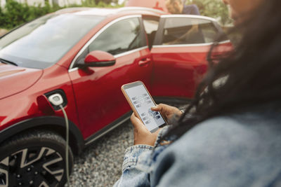 Woman using mobile app on smart phone near electric car