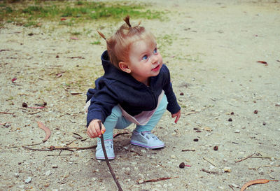 Baby girl holding stick while looking away against trees on field