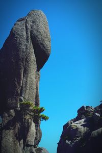 Low angle view of cliff against clear blue sky