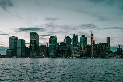 Sea by modern buildings in city against sky