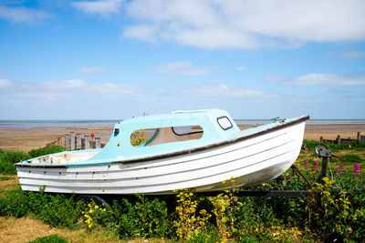 Little blue and white fishing boat out of water sitting amongst grass at top of beach 