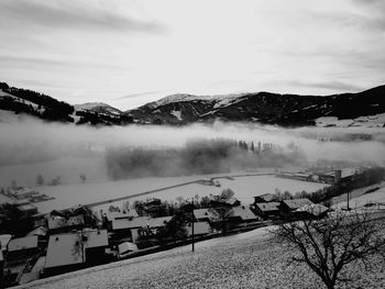 Fog over snow covered village against sky