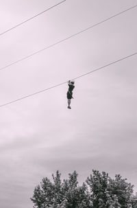Low angle view of person paragliding hanging on rope against sky