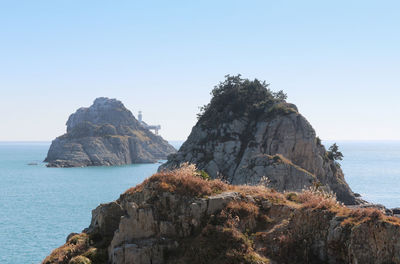 Rock formations by sea against clear blue sky