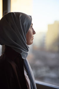 Thoughtful woman in headscarf looking through window