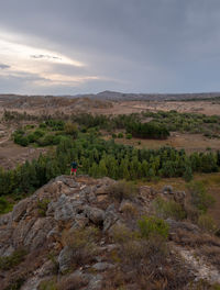 Scenic view of landscape with man standing on rock against sky