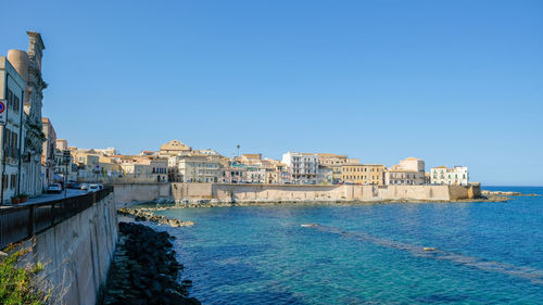 Buildings by sea against clear blue sky