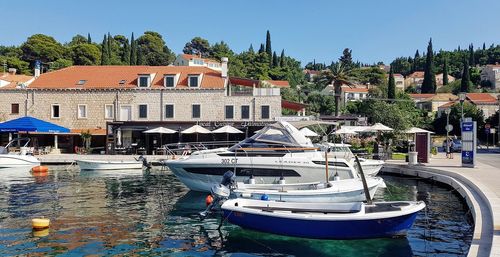 Boats moored in canal by buildings against clear blue sky