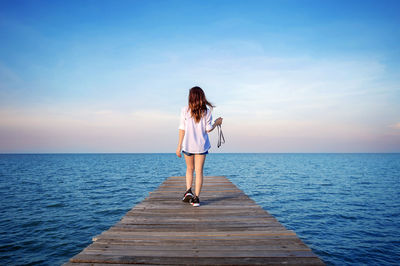Rear view of young woman standing on pier over sea against sky