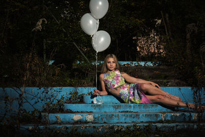 Portrait of young woman holding balloons lying on steps