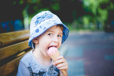 Portrait of cheerful boy eating ice cream while sitting on park bench