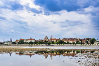 View of buildings by river against cloudy sky