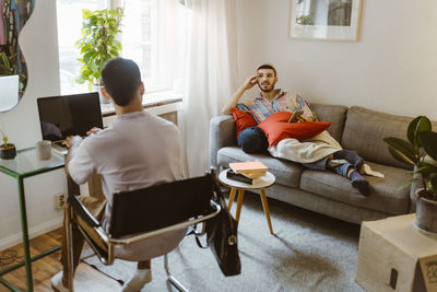 Man on sofa talking to boyfriend sitting with laptop at home