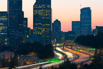 Light trails on road in illuminated city during sunset